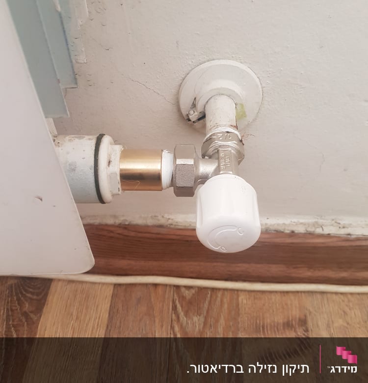 שסתום לבן מחובר לצינור מתכת בקיר